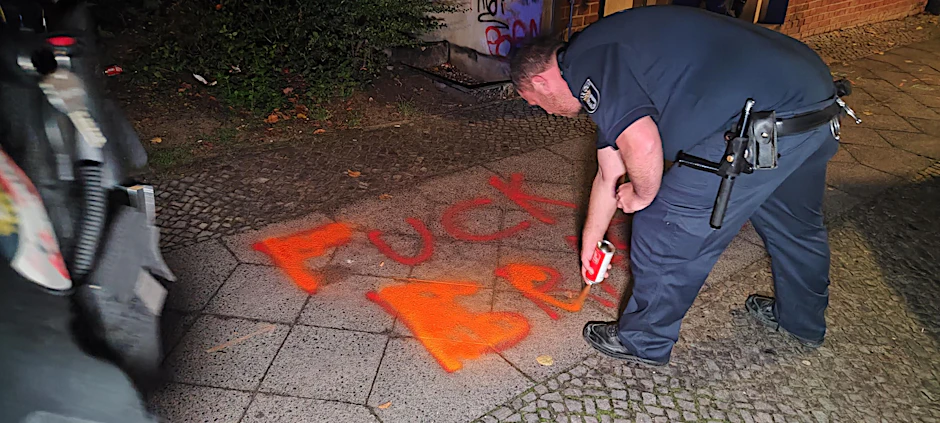 Hass-Parole auf einem Gehweg in Neukölln: Ein Polizist übersprüht sie mit Kreidespray.
