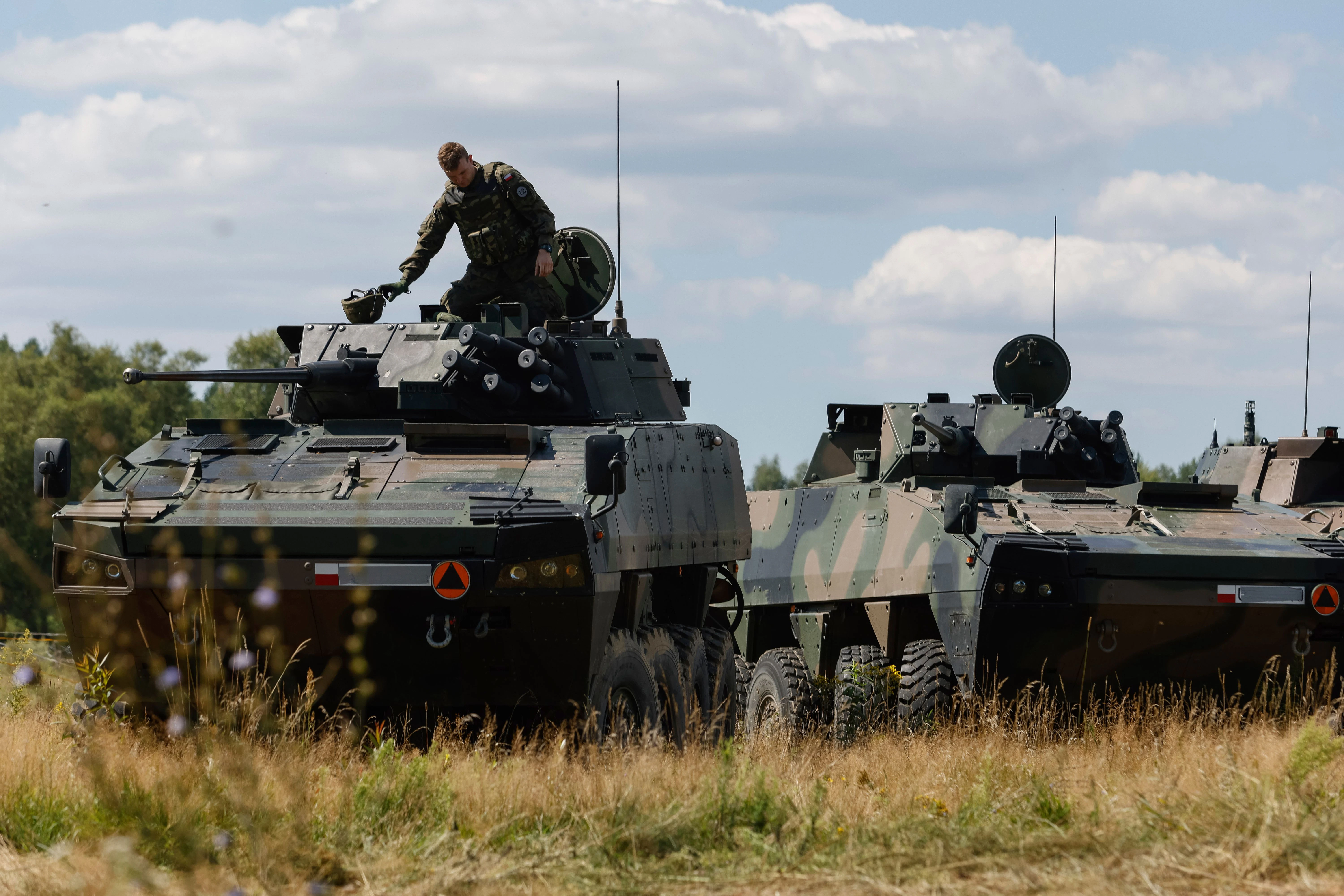 12.08.2023, Polen, Jarylowka: Ein polnischer Soldat sitzt auf einem gepanzerten Fahrzeug vor einer Pressekonferenz von Polens Verteidigungsminister Blaszczak.