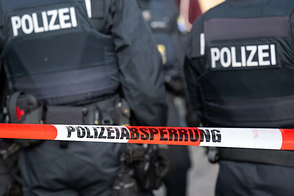 Polizisten stehen hinter einem Polizei-Flatterband.  
