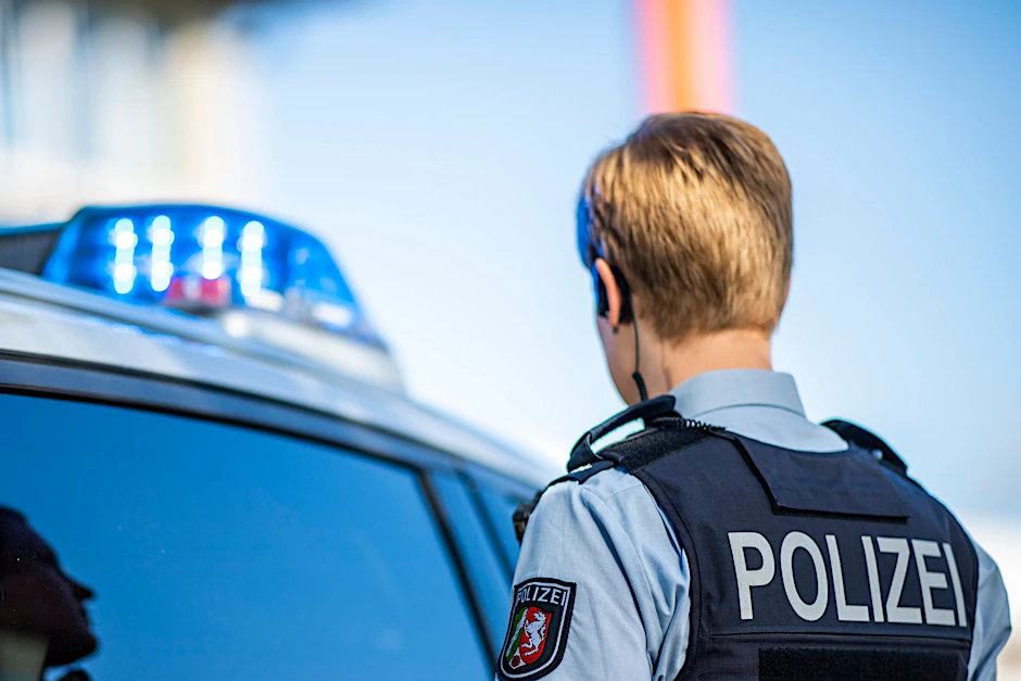 ILLUSTRATION - Eine Polizistin steht vor einem Streifenwagen.  