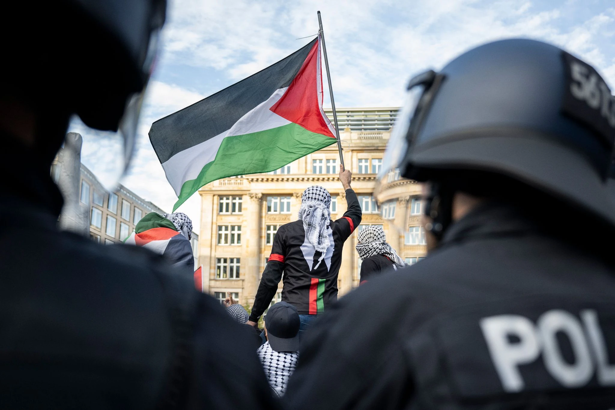 Ein Teilnehmer einer verbotenen Pro-Palästina-Demonstration in Frankfurt am Main schwenkt eine Palästina-Flagge, während Polizisten die Situation beobachten.  