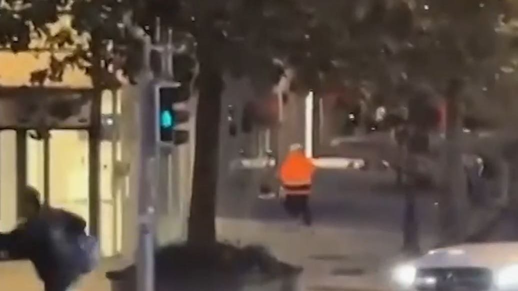 Mit einem Gewehr in der Hand läuft der Mann über den Bürgersteig.