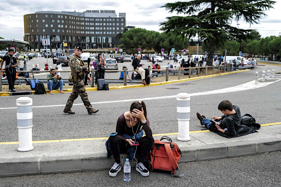 Reisende warten, während ein französischer Soldat vor dem Flughafen Toulouse-Blagnac patrouilliert. 