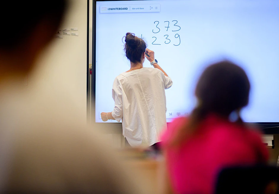 ARCHIV - Eine Lehrerin schreibt eine Mathematikaufgabe auf eine digitale Schultafel im Klassenraum einer 4. Klasse einer Grundschule.  