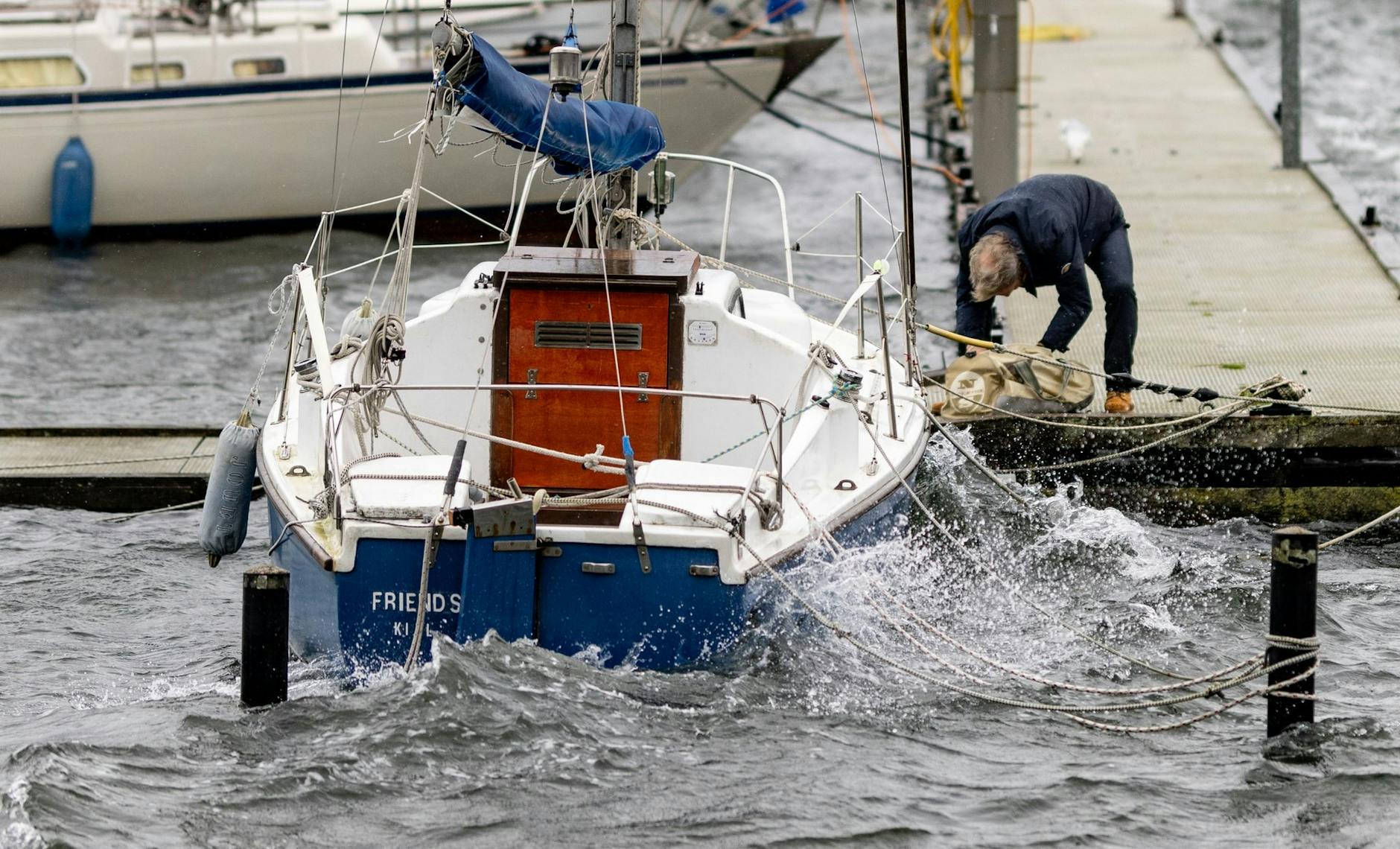 Ein Mann sichert ein Segelboot an einem Anlegesteg in der Kieler Förde.