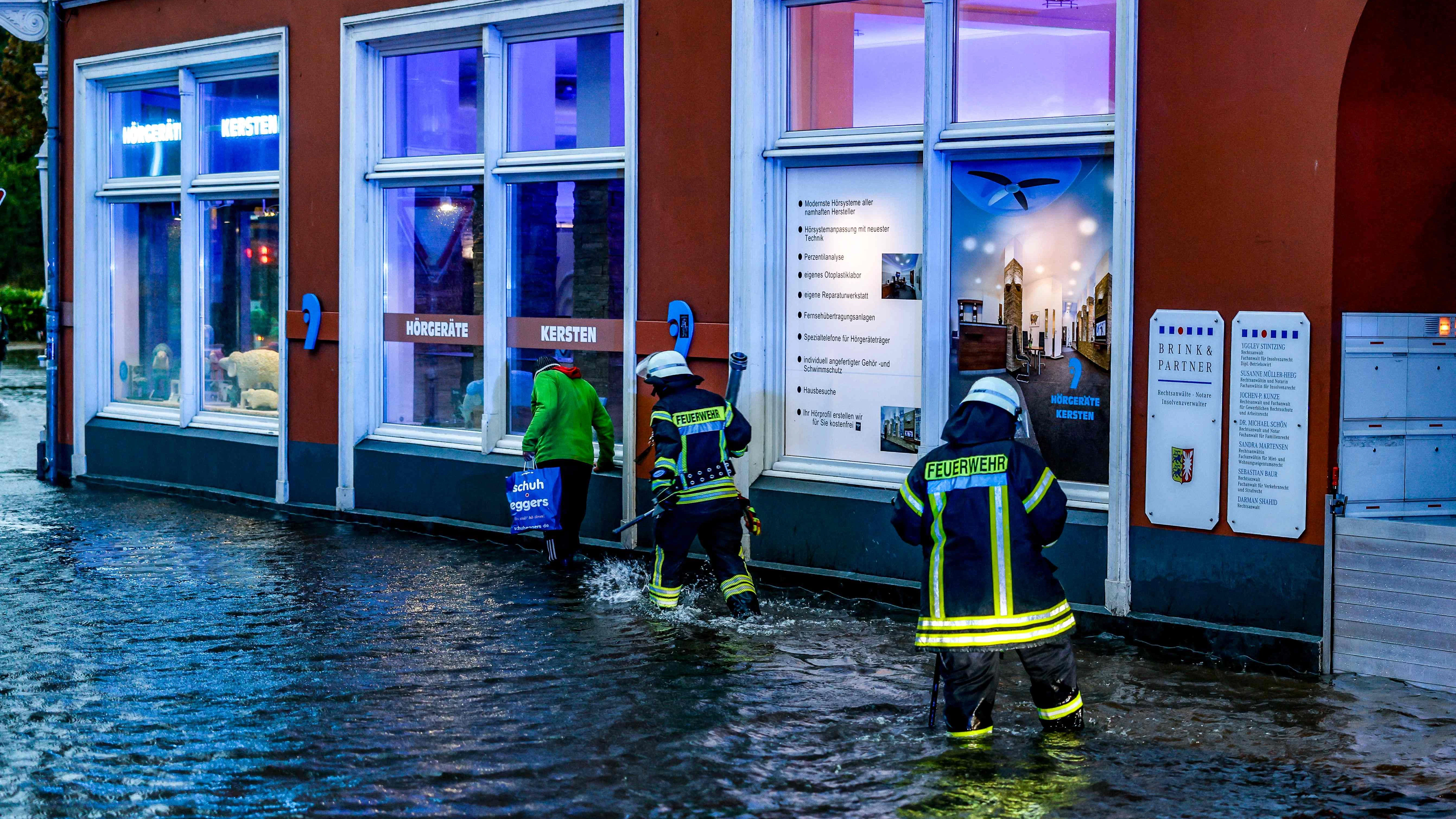 Feuerwehrleute und eine Passantin auf einer völlig überfluteten Straße in Flensburg.&nbsp;