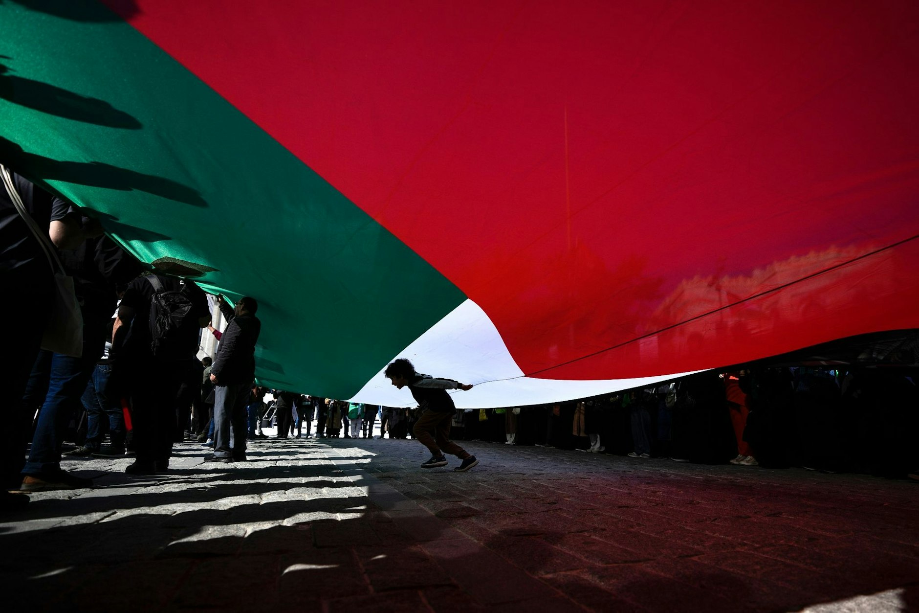 dpatopbilder - Ein Junge geht in Istanbul, während einer Demonstration zur Solidarität mit den Palästinensern, unter einer riesigen palästinensischen Fahne hindurch.  