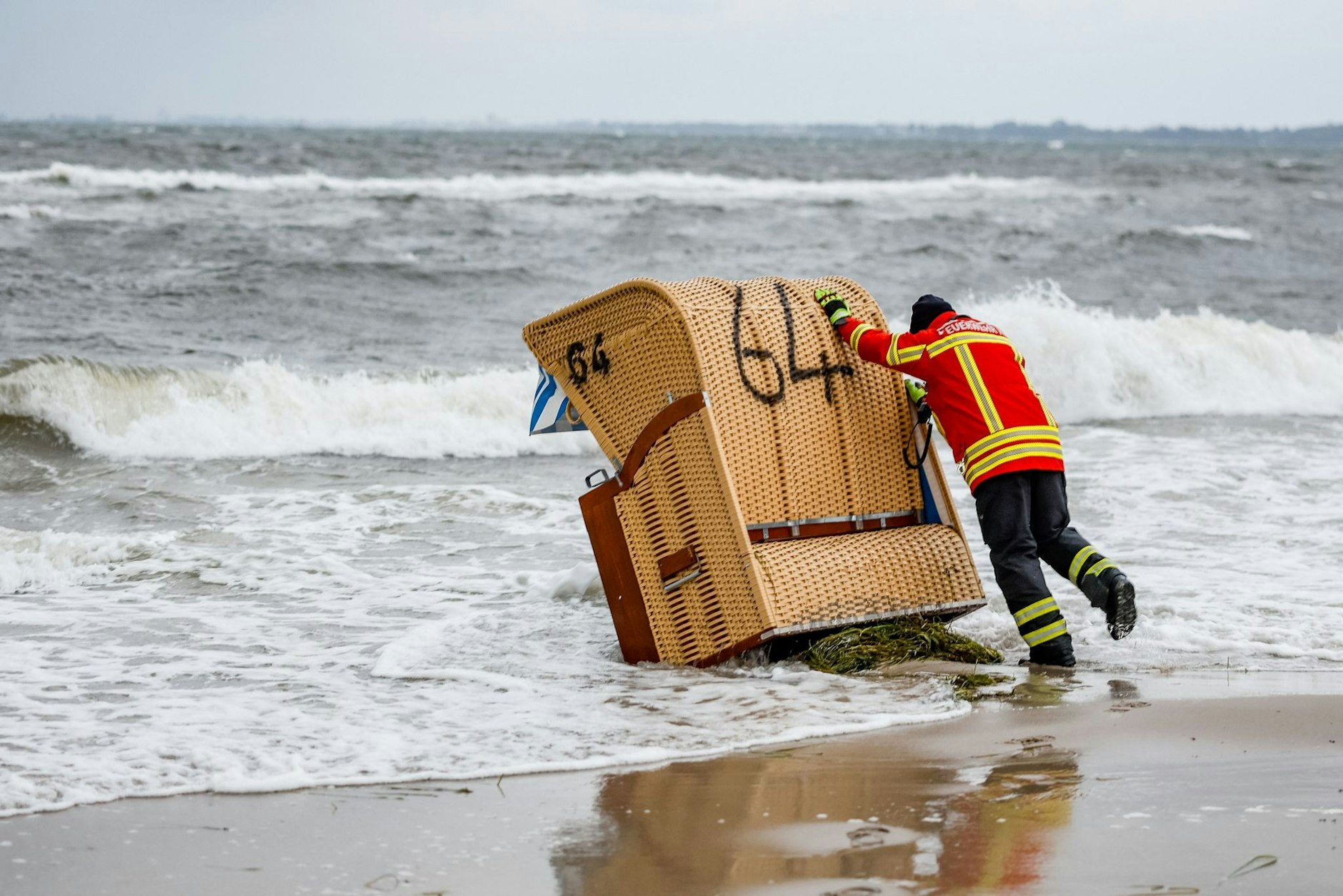Ein Feuerwehrmann versucht, in Kiel-Schilksee einen Strandkorb vor den Flutwellen der Ostsee zu sichern.  