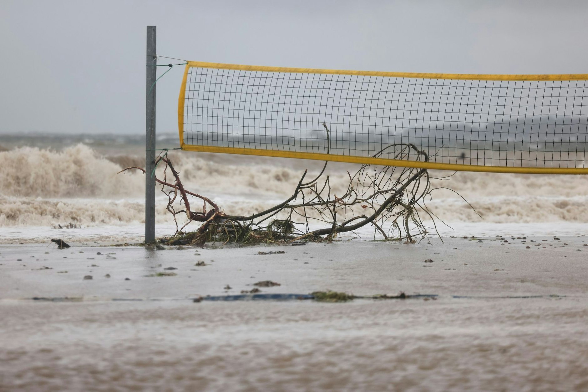 Ein entwurzelter Baum liegt unter einem Volleyballnetz am Ostseestrand von Eckernförde.  