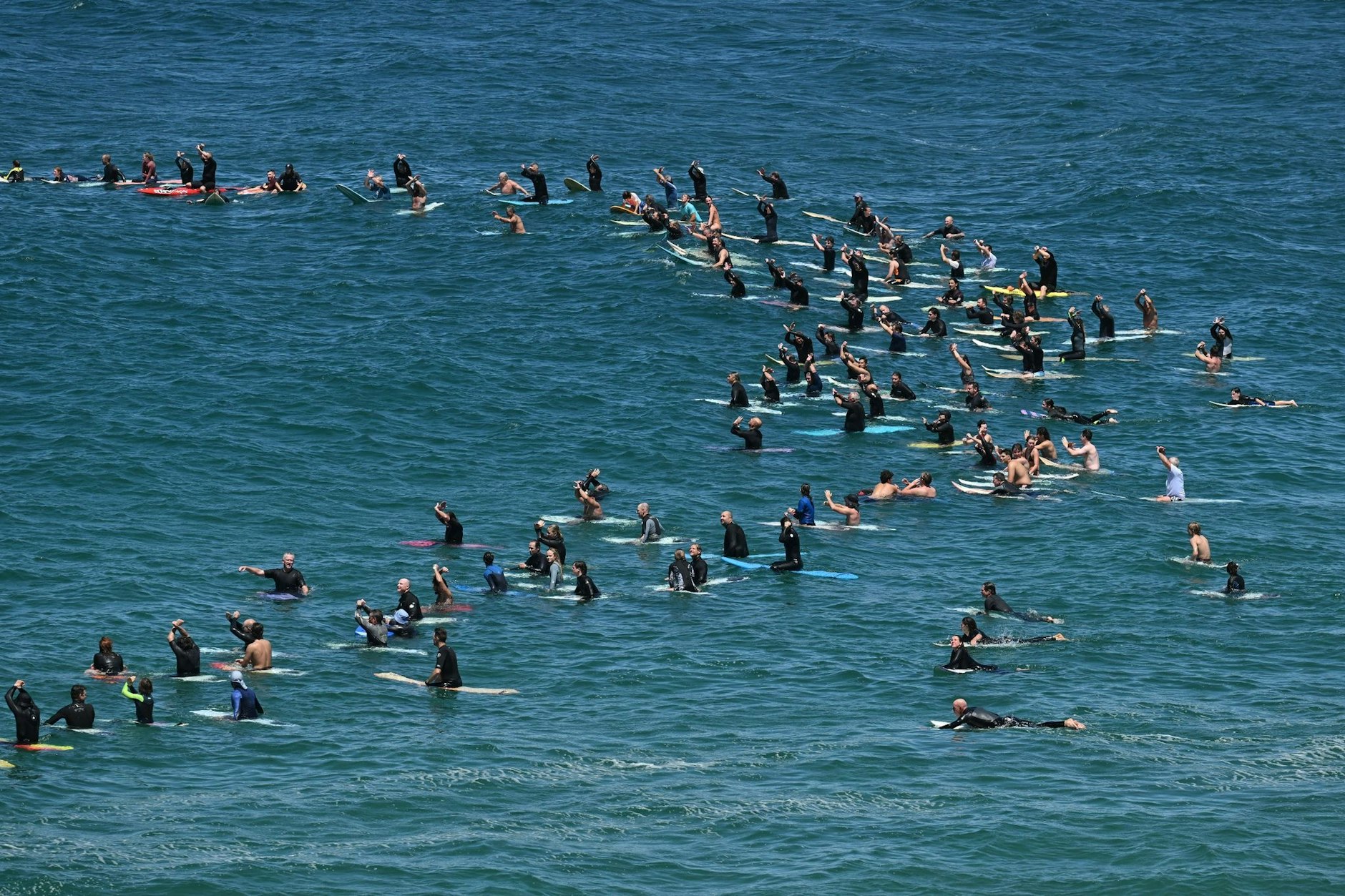 Surfer paddeln am Wollongong Main Beach in Australien nach einer Kundgebung gegen einen geplanten Offshore-Windkraftpark im Wasser.  