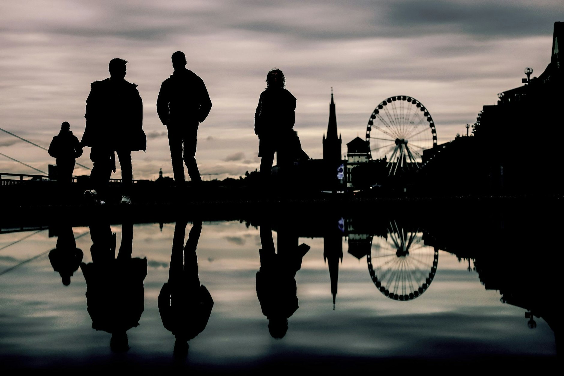 Spaziergänger spiegeln sich bei grauem Himmel am Düsseldorfer Rheinufer in einer Pfütze. Ein typisches Bild in diesem Monat: Laut der Bilanz des Deutschen Wetterdienstes war es der regenreichste Oktober seit 2002.