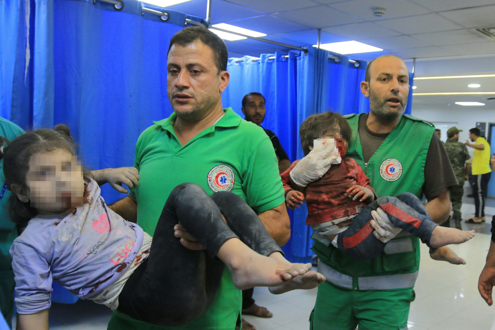 Im Al-Shifa-Hospital gibt es keine klare Abgrenzung zwischen zivilen Kräften und Angehörigen des Militärs: zwei Sanitäter mit Emblemen der palästinensischen Militärverwaltung mit verletzten Kindern. Im Hintergrund ein uniformierter Soldat.