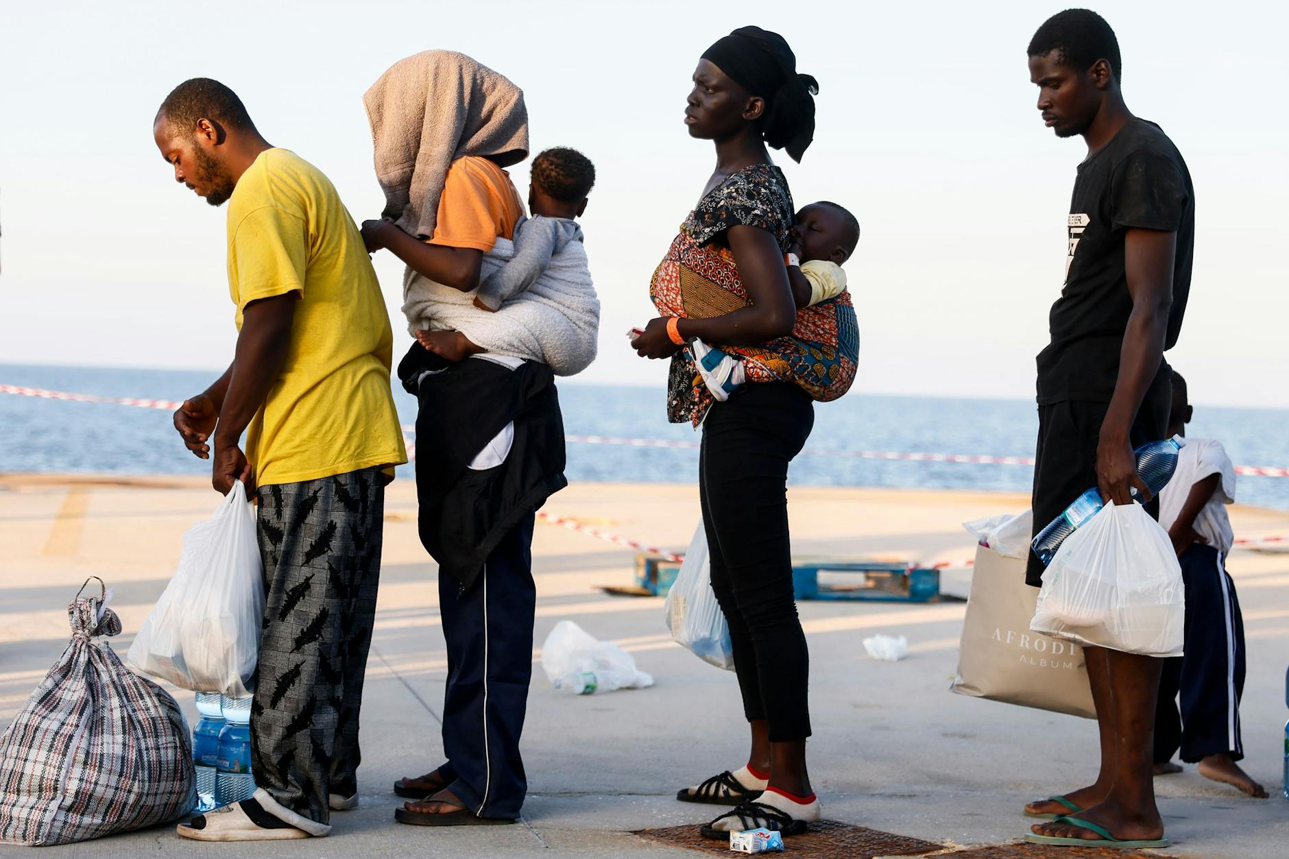 I migranti aspettano di essere trasferiti su una nave diretta dall'isola di Lampedusa verso l'Italia continentale.