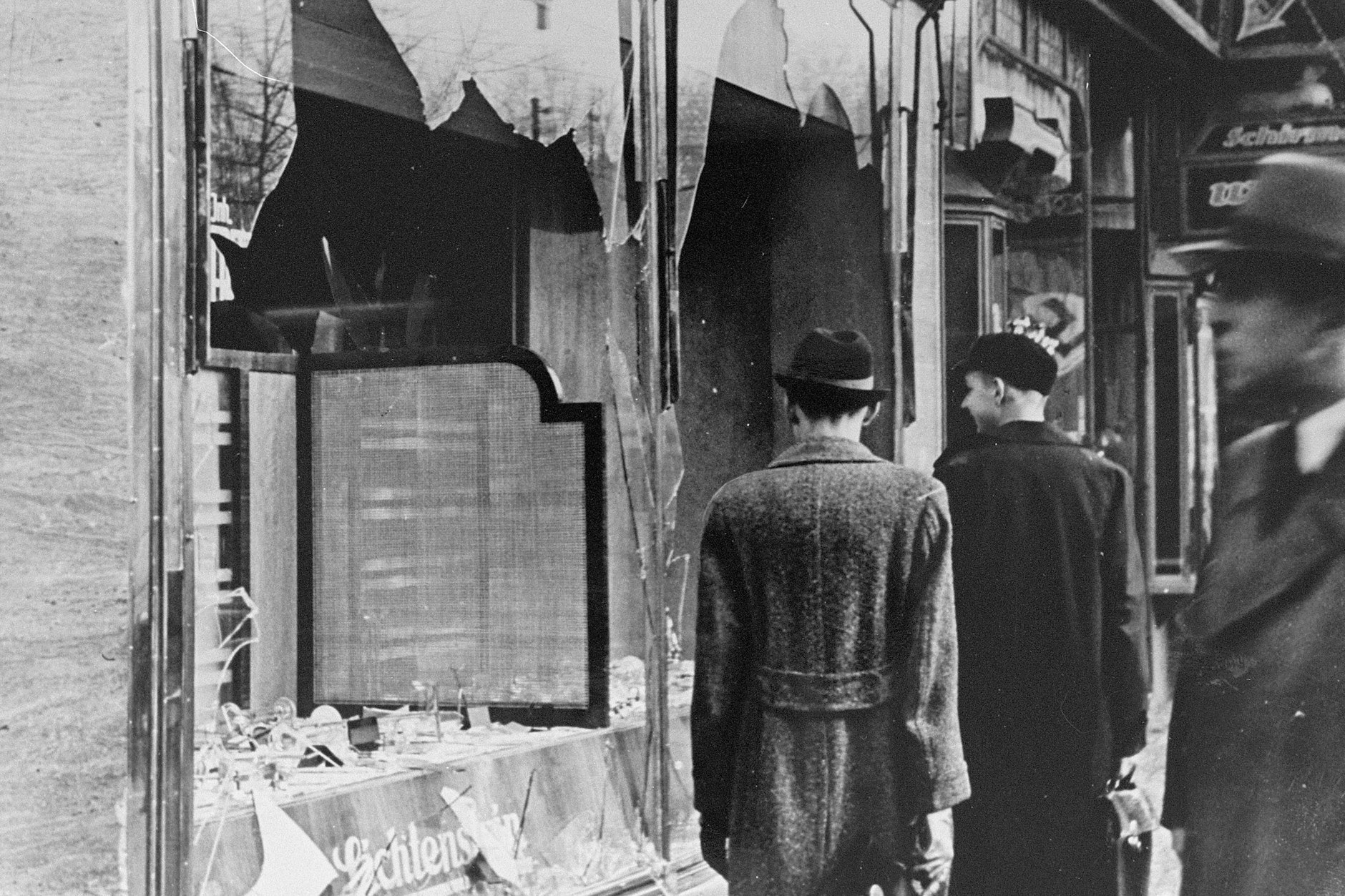 Passanten gehen nach der Pogromnacht vom 9. auf den 10. November 1938 an einem zerstörten Schaufenster eines jüdischen Geschäfts vorbei. 