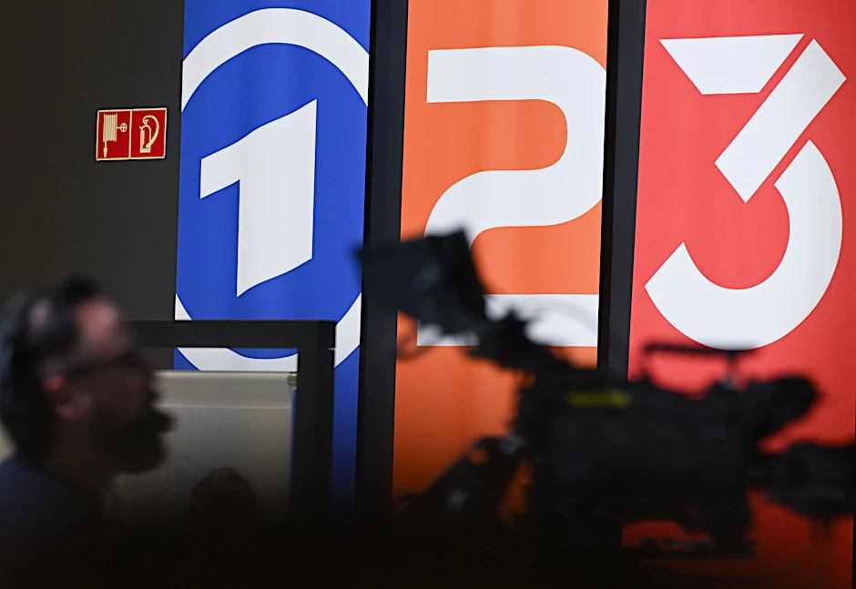 Fahnen mit den Markenlogos von ARD, ZDF und 3sat sind im Oktober 2023 im Hintergrund einer TV-Kamera auf der Frankfurter Buchmesse zu sehen.