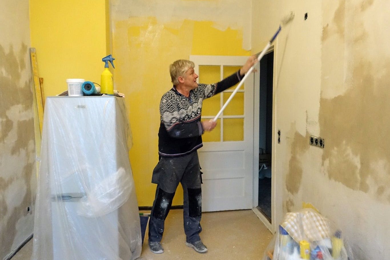 Ein Mann streicht in seiner Wohnung eine Küchenwand.