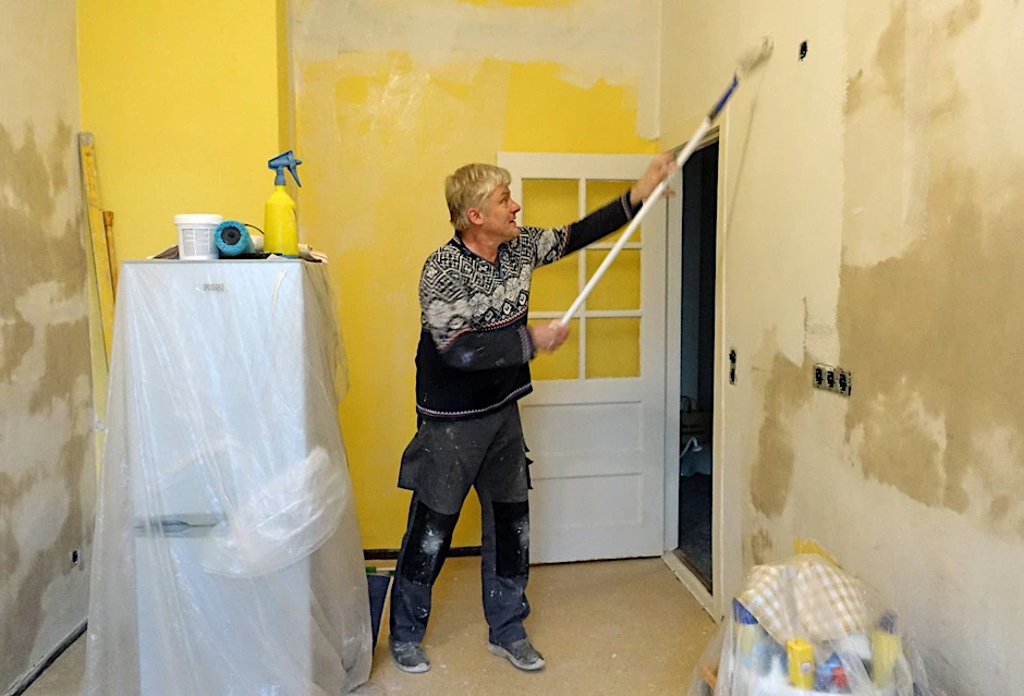 Ein Mann streicht in seiner Wohnung eine Küchenwand.