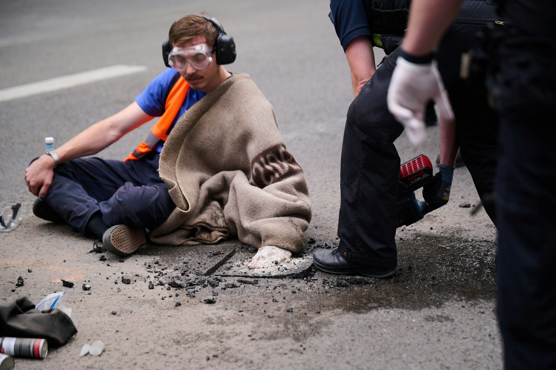 Ein Aktivist der Klimaschutzgruppe Letzte Generation klebt mit seiner Hand auf der Friedrichstraße, während Polizisten versuchen, den Asphalt unter seine Hand zu entfernen.