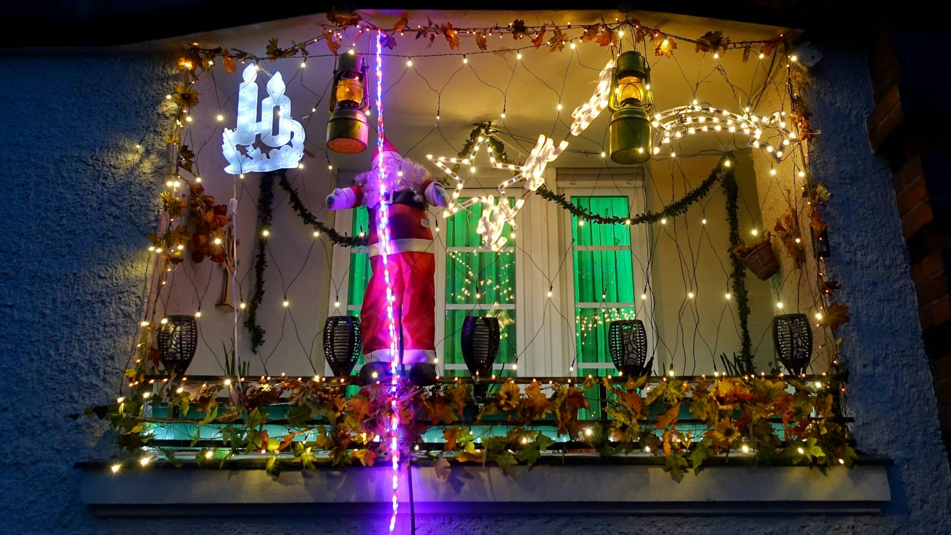 Ein festlich dekoriertes Fenster mit Weihnachtsmann am neonfarbenen Seil in der Vorweihnachtszeit.