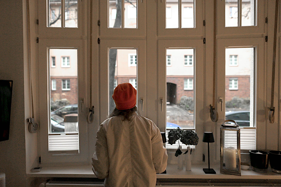 Melanie G. möchte unerkannt bleiben. Sie steht mit Jacke und Mütze in ihrer Wohnung, weil sie friert.