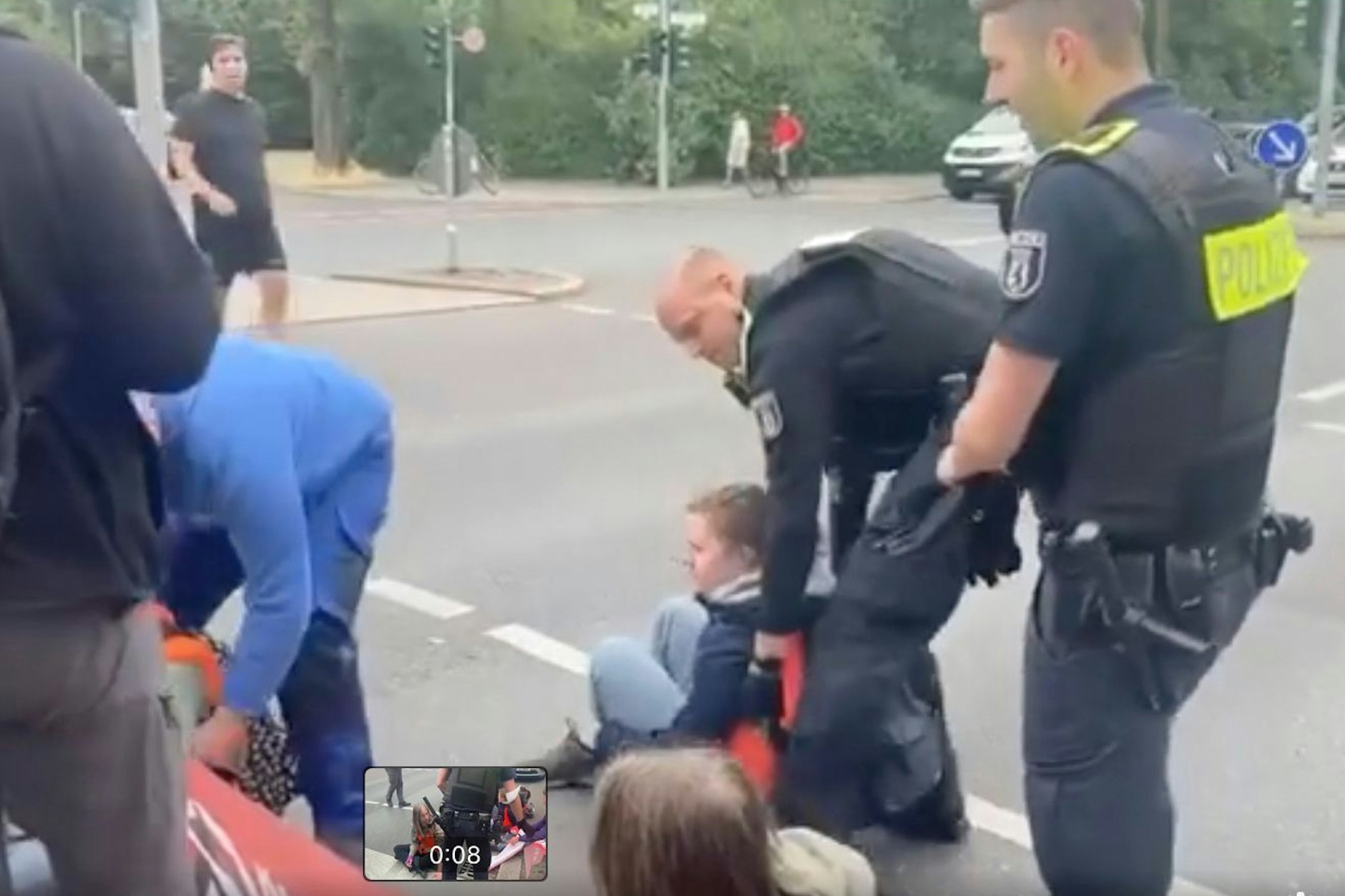 Der Autofahrer links im Blaumann hebt die Frau unter den Achseln an. Die Polizisten machen mit.