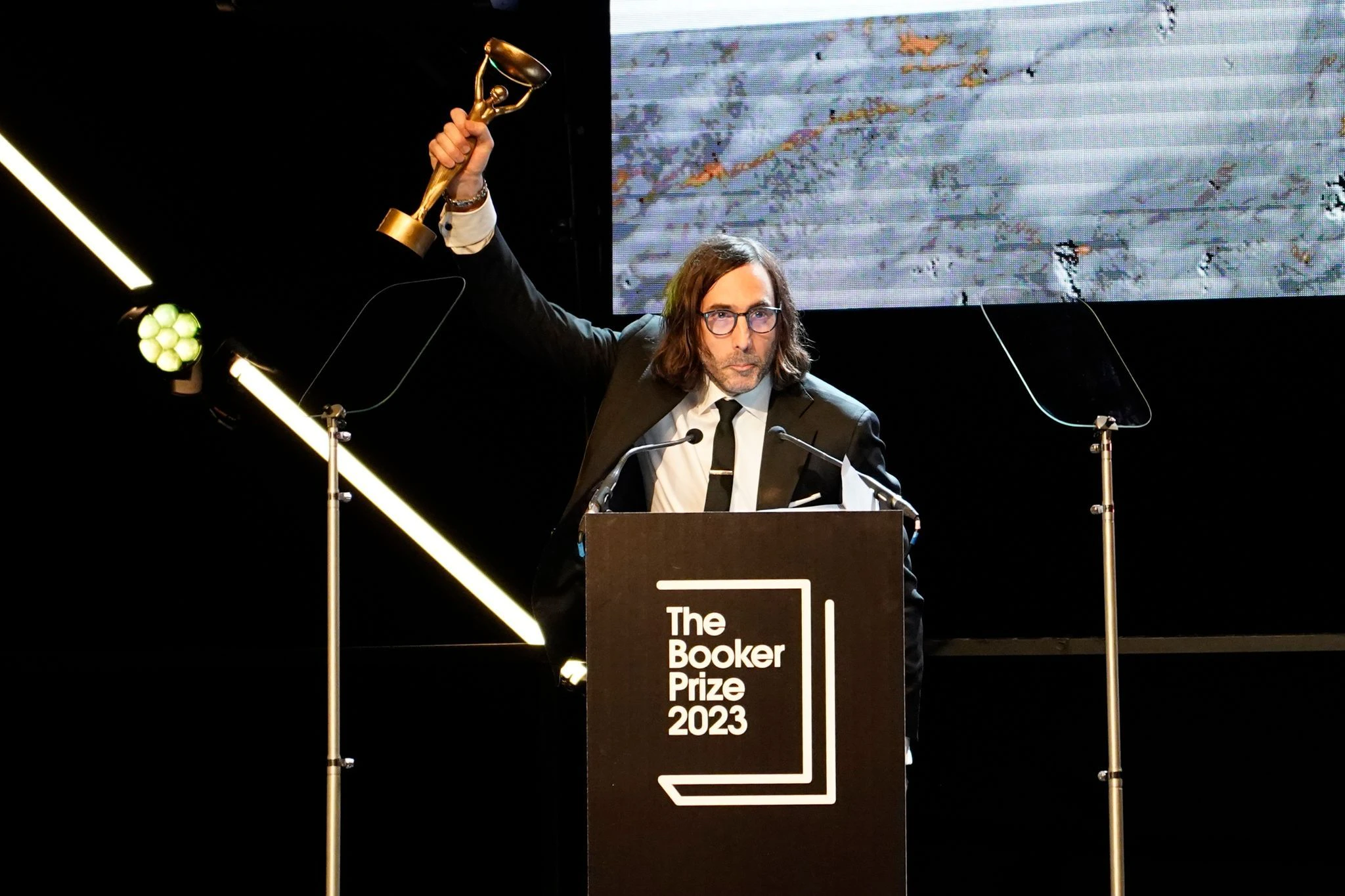 Der Booker Prize wird für das nach Meinung der Jury beste nachhaltige belletristische Werk verliehen, das auf Englisch im Vereinigten Königreich und Irland publiziert wurde. Paul Lynch überzeugte mit einer dystopischen Vision von Irland in den Fängen des Totalitarismus - und jubelt auf der Bühne.  