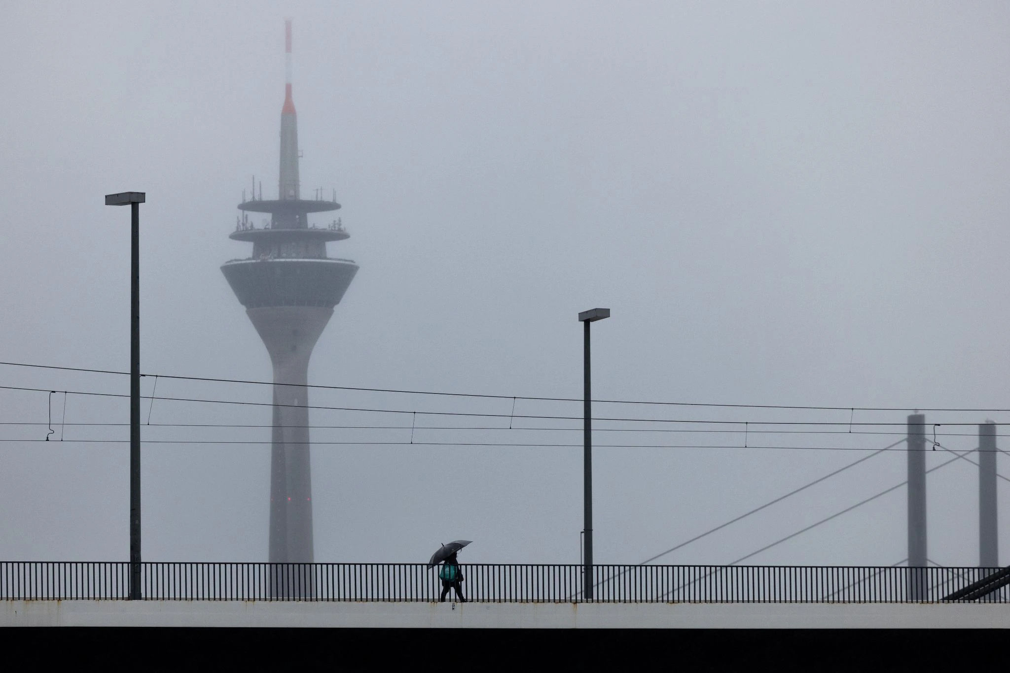 PRODUKTION - Während es mancherorts schneit, dominieren in Düsseldorf graue Nebelsuppe und Regen das Wetter. Eine Person wagt sich trotzdem an die frische Luft - wenn auch nur mit Regenschirm.  