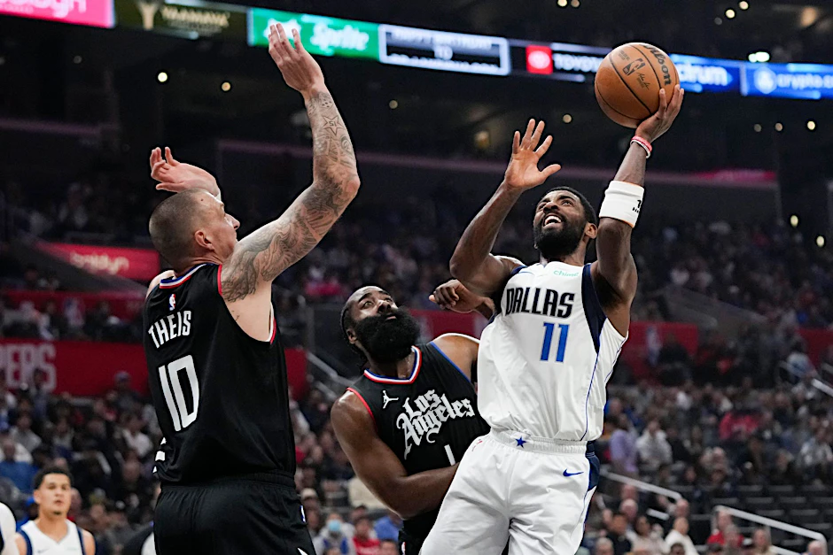 Kyrie Irving (r) von den Dallas Mavericks wirft unter dem Druck von James Harden (M) und Daniel Theis von den Los Angeles Clippers.  