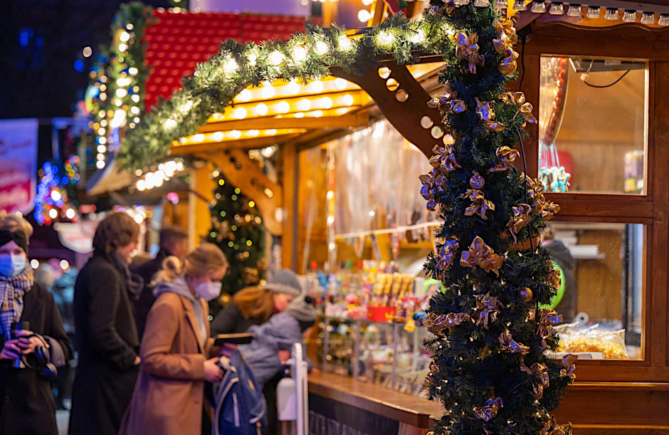 Besucher eines Weihnachtsmarktes stehen an einem Verkaufsstand für Süßigkeiten.  ld/dpa/Symbolbild