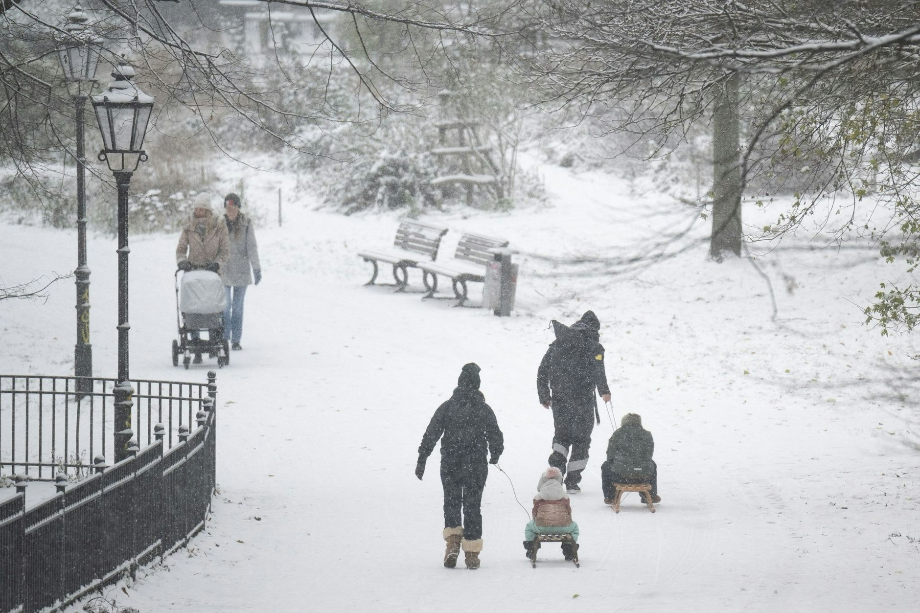 Menschen spazieren durch den verschneiten Volkspark Friedrichshain in Berlin.  