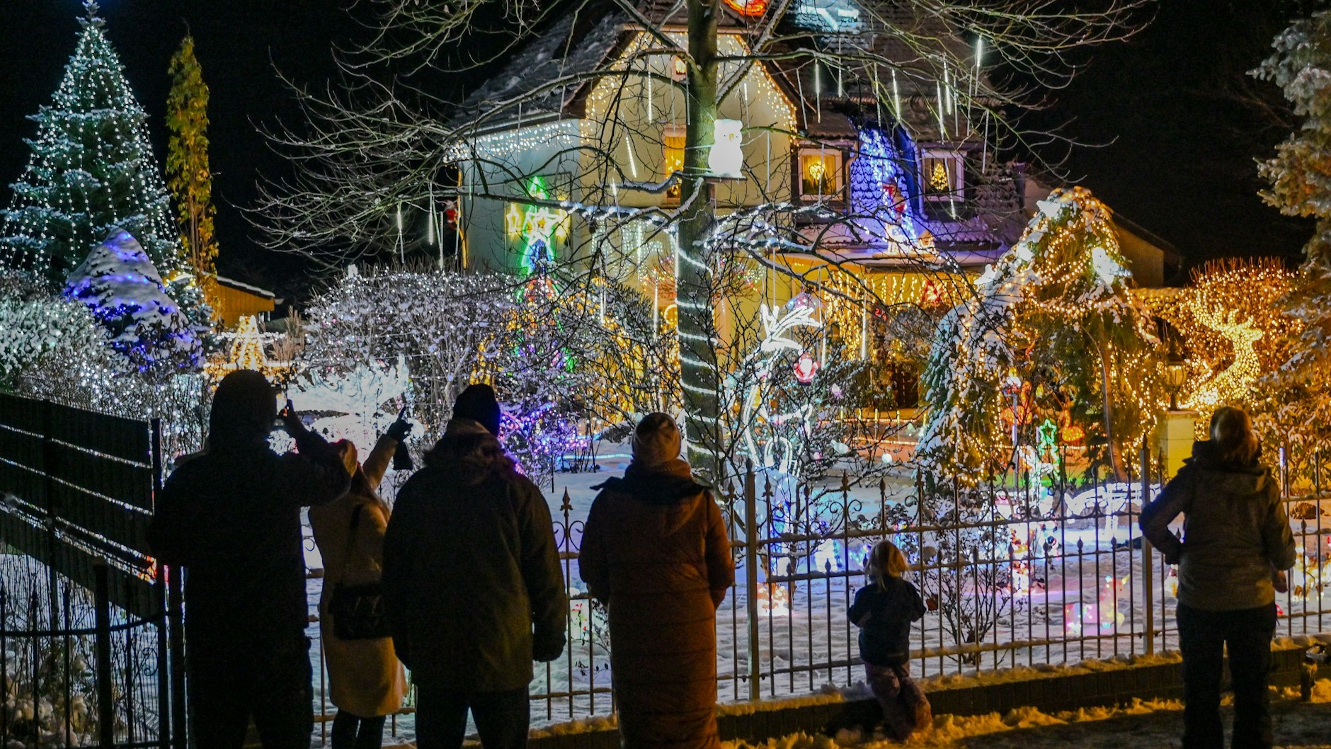 Schaulustige stehen vor dem weihnachtlich hell beleuchteten Garten der Familie Muschner in Ostbrandenburg. Etwa 20 Zeitschaltuhren sorgen dafür, dass sich das Anwesen samt Hausfassade in ein leuchtendes Weihnachtsparadies verwandelt.