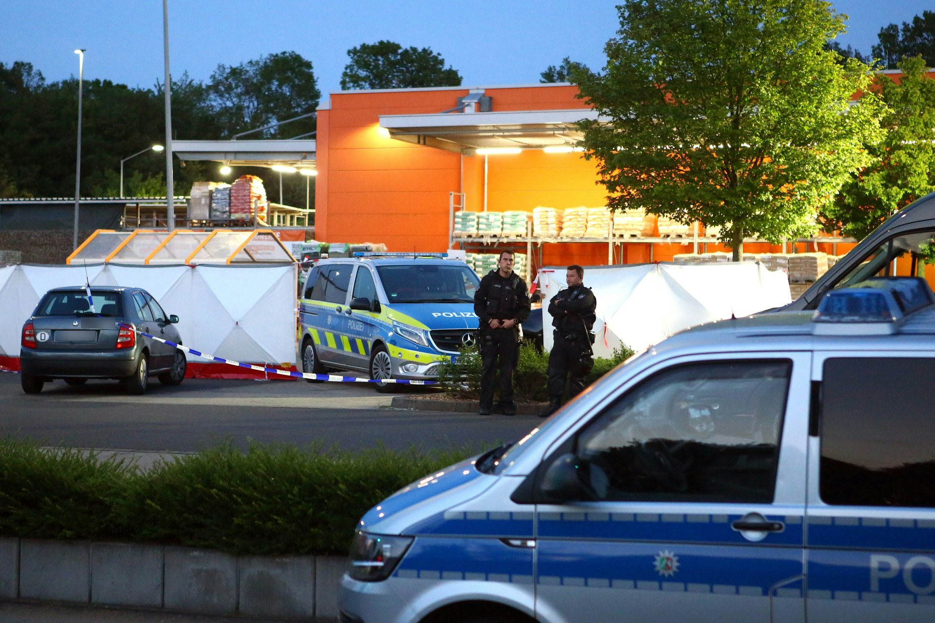 Polizisten stehen am Tatort auf dem Parkplatz eines Baumarkts.