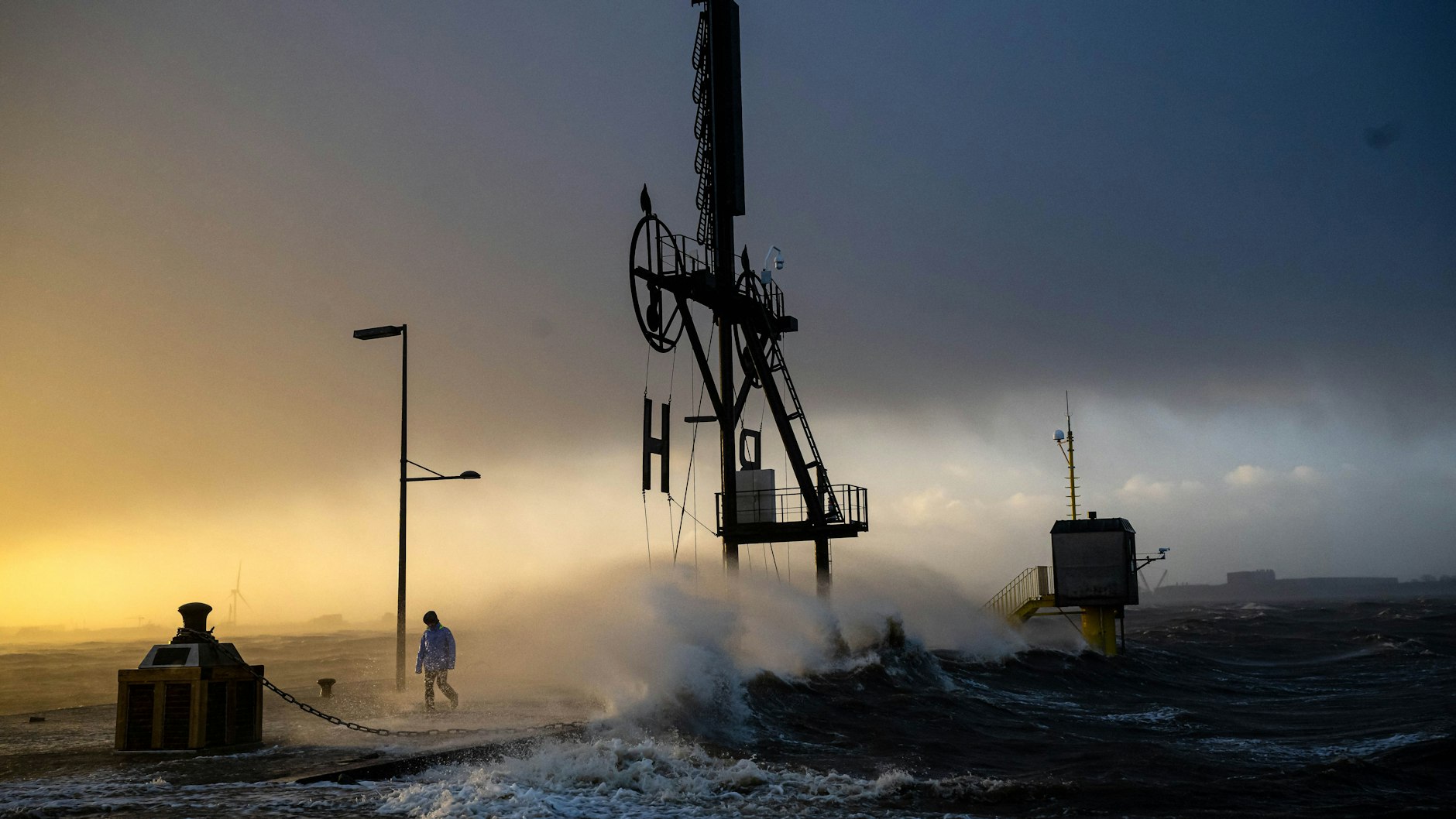 Ein Spaziergänger läuft bei Sturmflut und Wellen am Ufer der Wesermündung in Bremerhaven.