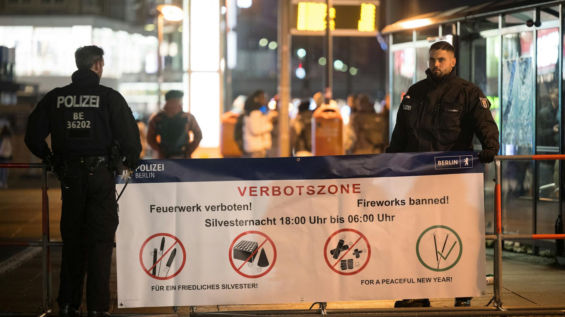 Polizeibeamte stehen an der Böllerverbotszone am Alexanderplatz an einem Hinweisschild.
