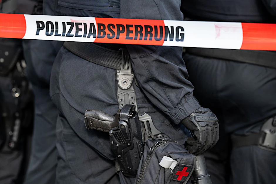 Polizisten stehen hinter einem Polizei-Flatterband.  