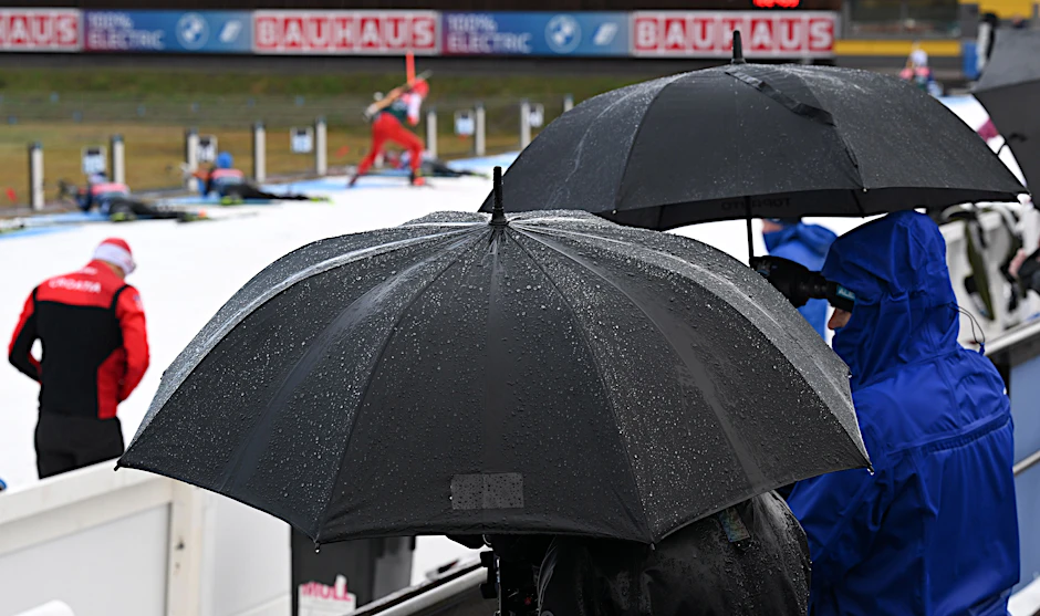 Trainer unter Schirmen beobachten Biathleten im Training bei Dauerregen vor dem Biathlon-Weltcup in der Arena von Oberhof.