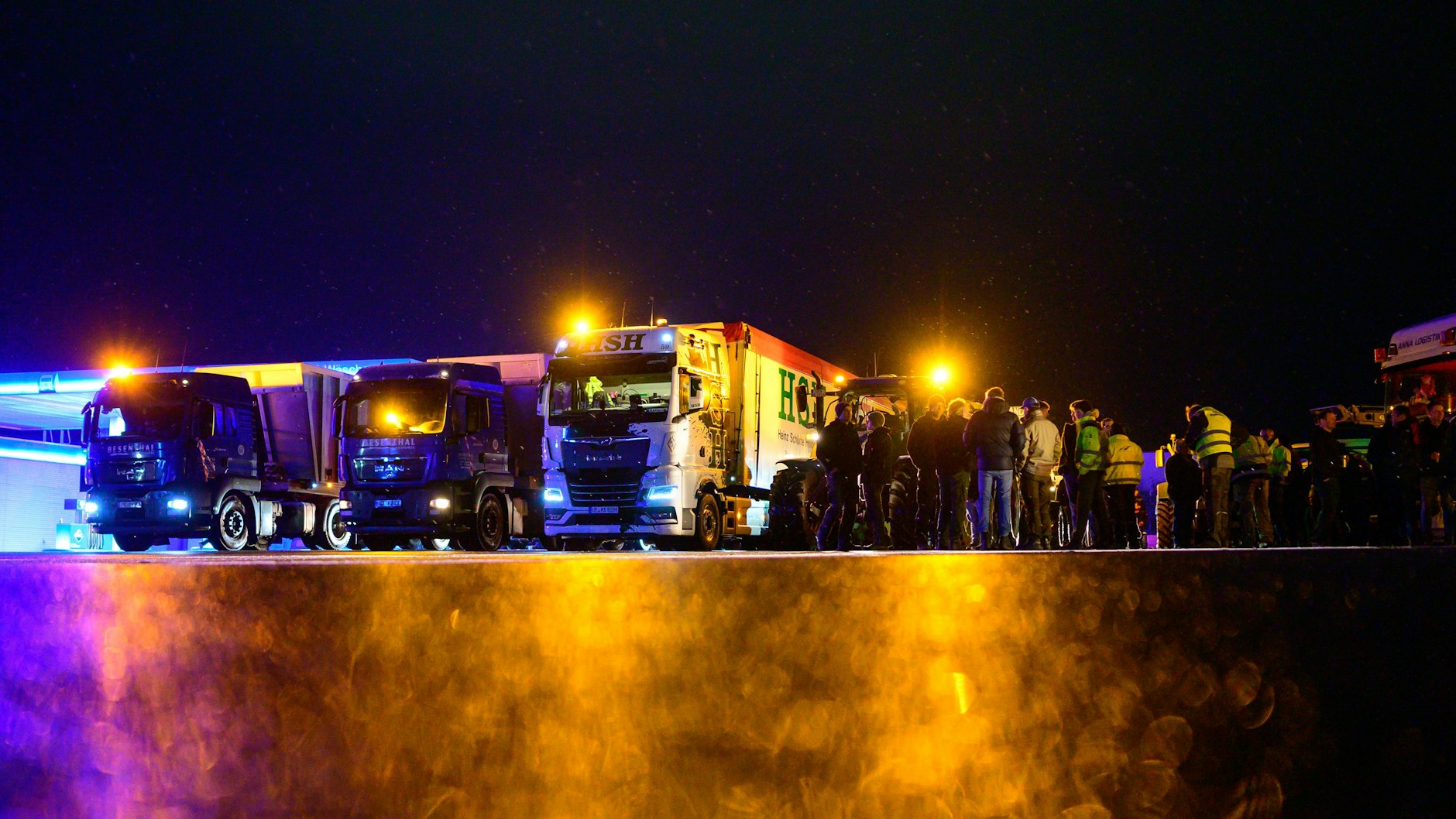 Landwirte stehen zusammen mit Lkw-Fahrern an einem Sammelplatz, kurz bevor sie zum Bauernprotest starten. 