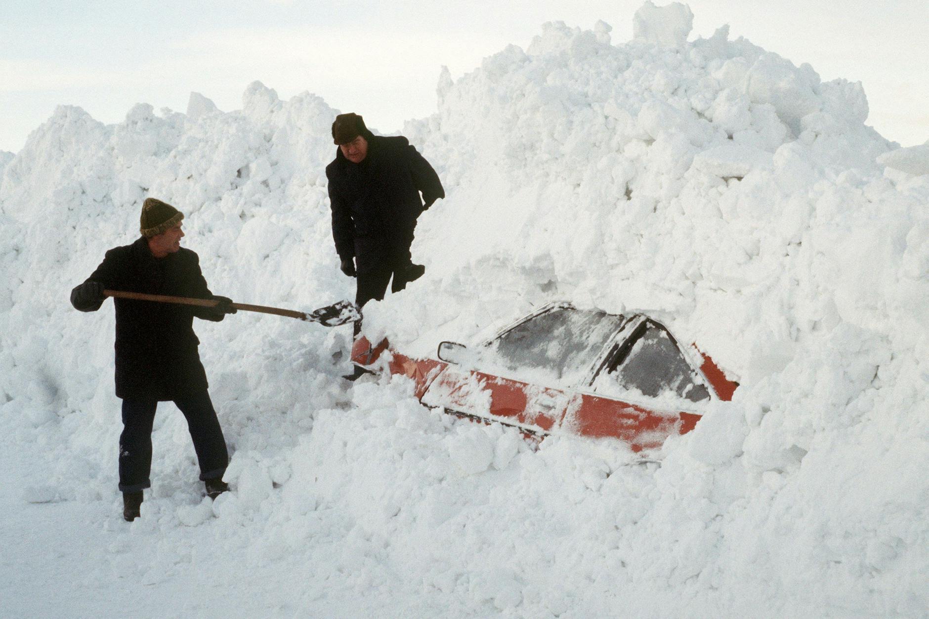 Zwei Männer schaufeln ein Auto aus den Schneemassen frei.