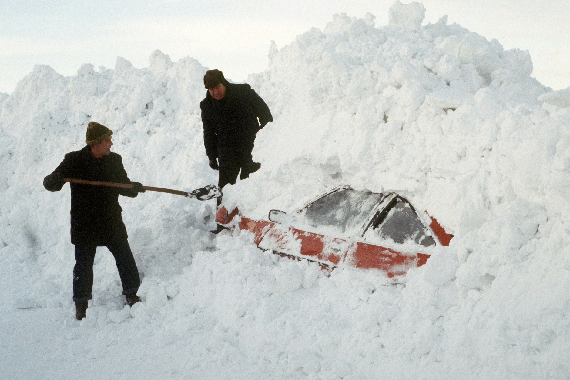 Zwei Männer schaufeln&nbsp;ein Auto aus den Schneemassen frei.