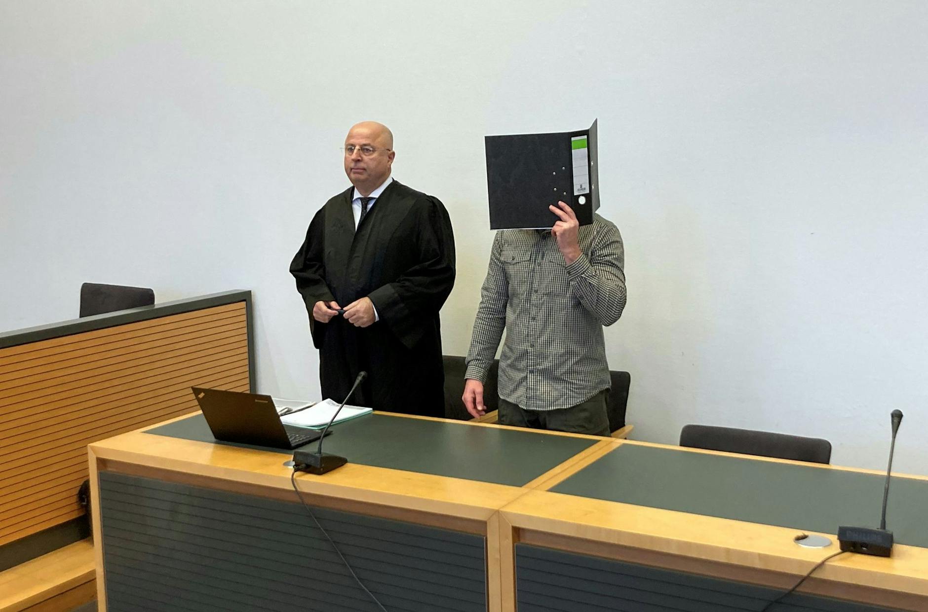 Der Angeklagte steht neben seinem Anwalt im Gerichtssaal.