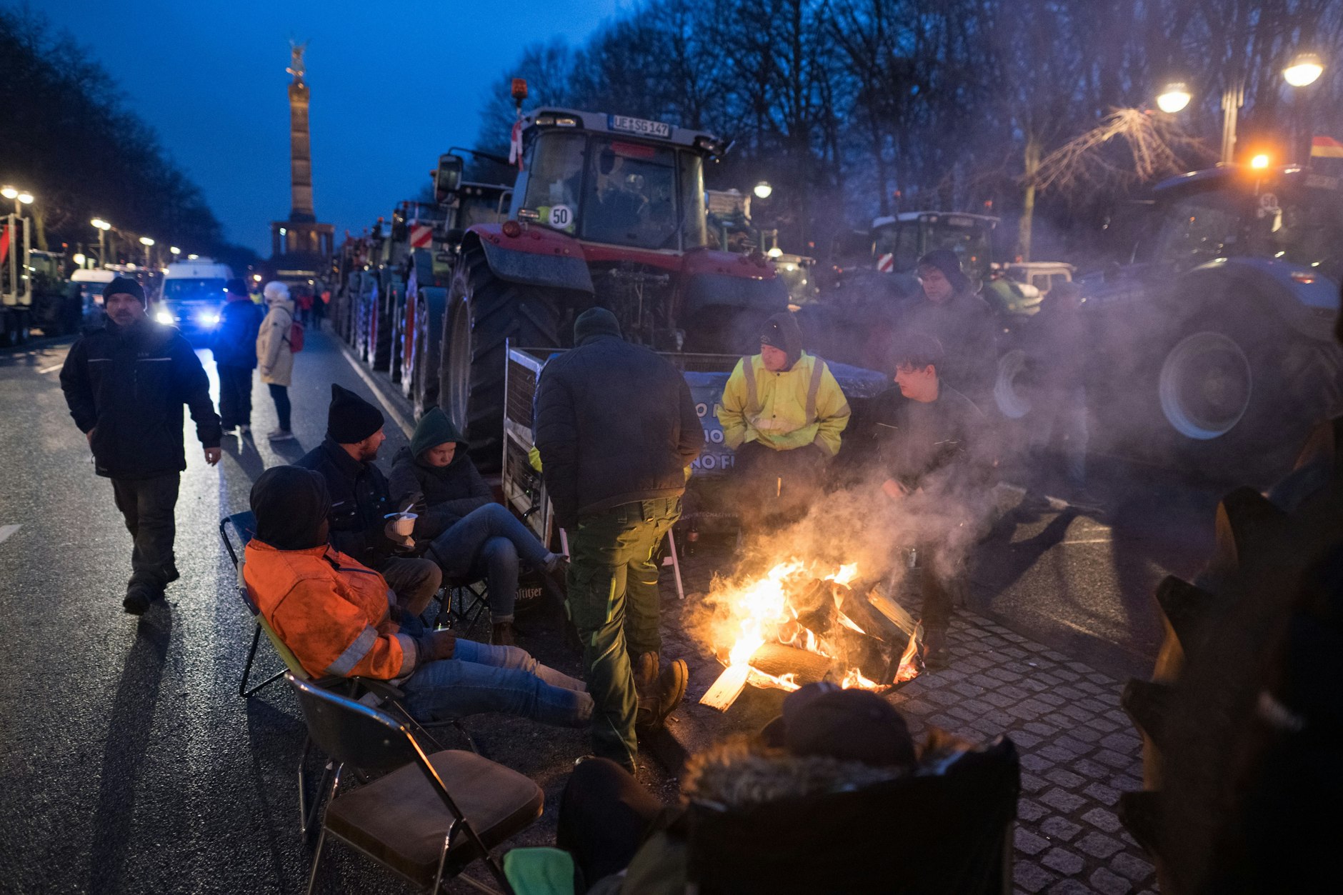Landwirte und andere Unternehmer sitzen am Brandenburger Tor zwischen Traktoren an einem Feuer. 