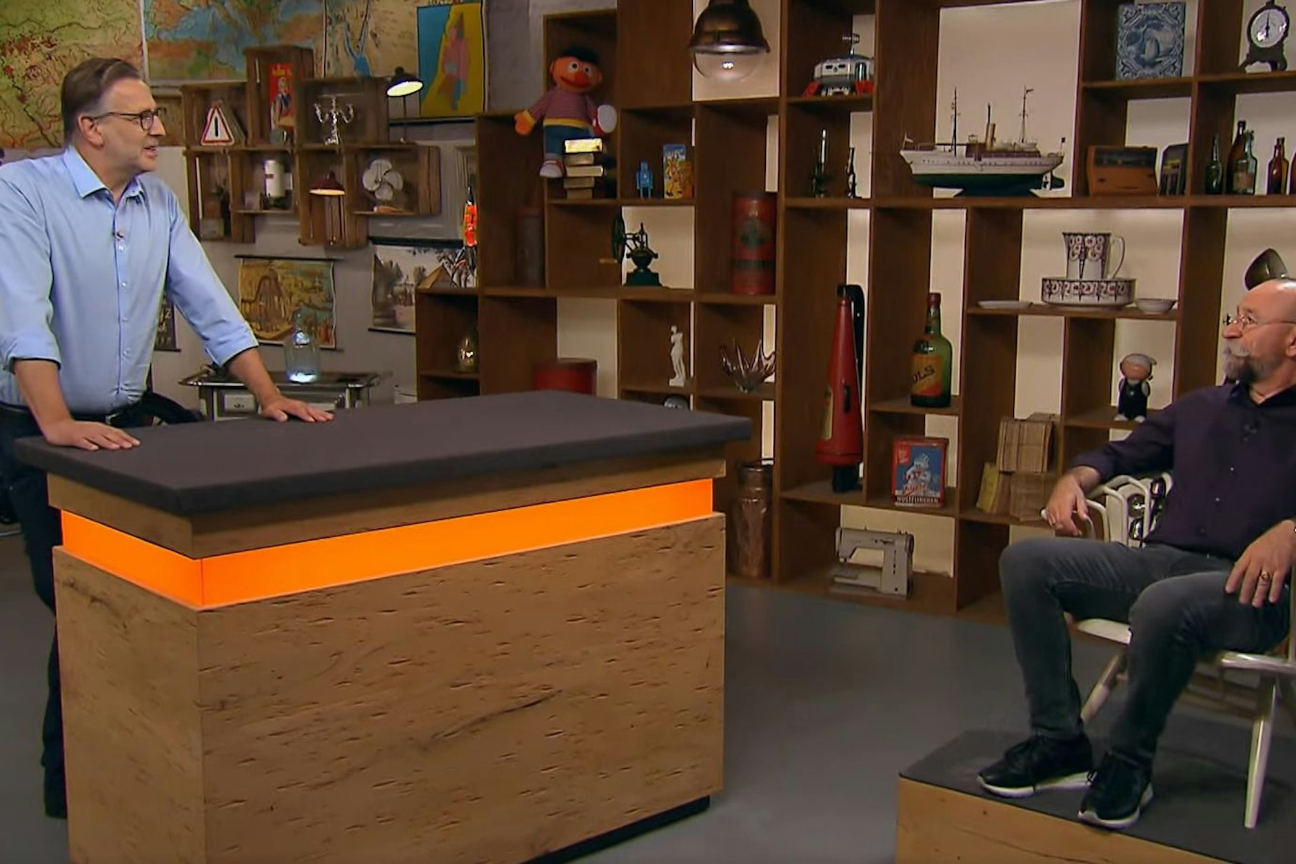 „Bares für Rares“-Moderator Horst Lichter (r.) probiert den alten Designerstuhl gleich mal aus. Dabei handelt es sich laut Expertenmeinung von Detlev Kümmel (l.) aber um einen Sessel.