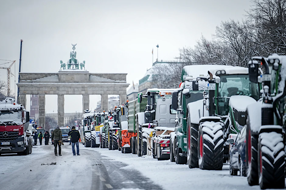 Zahlreiche schneebedeckte Traktoren stehen auf der Straße des 17. Juni vor dem Brandenburger Tor.