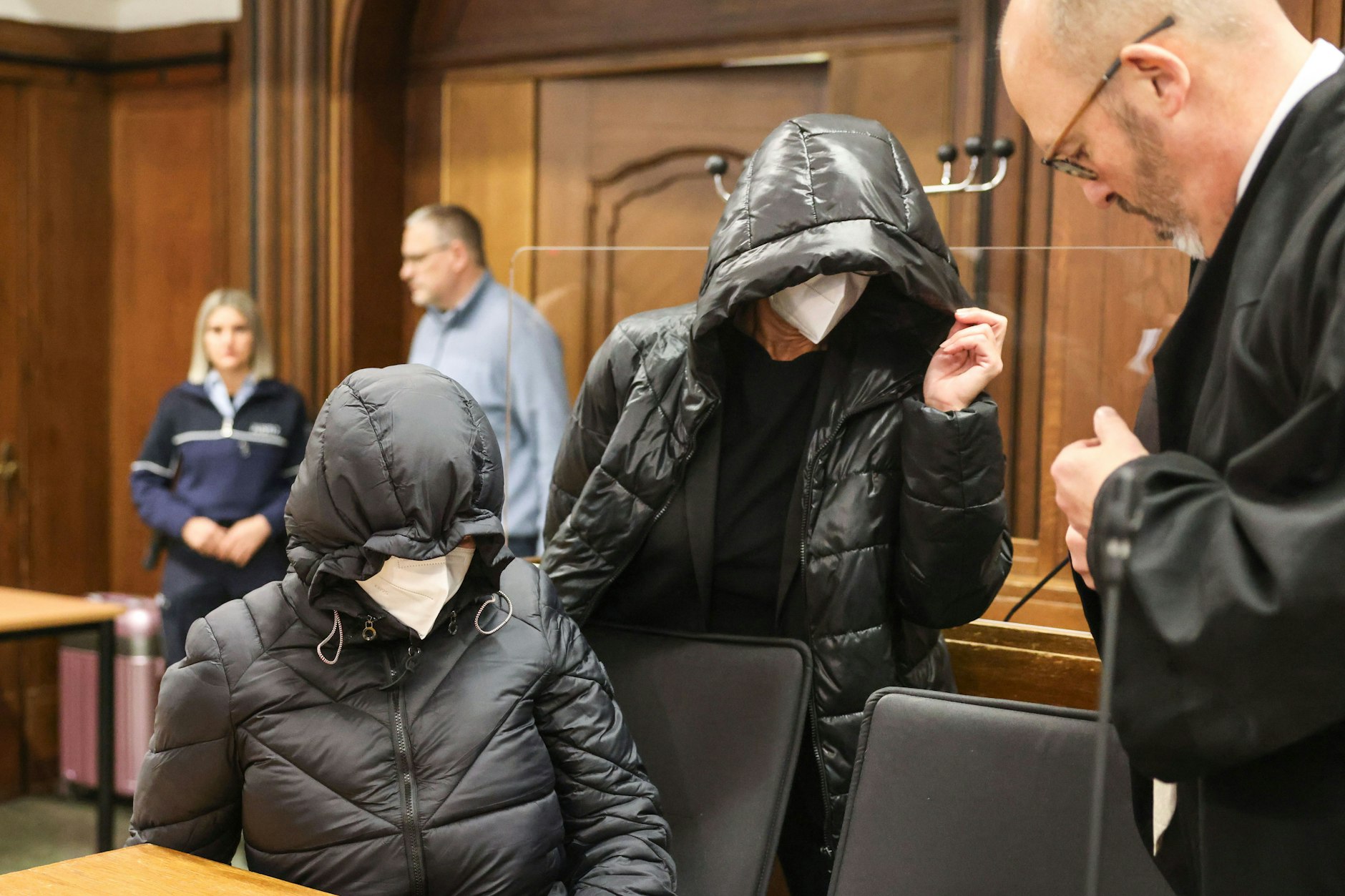 Die beiden angeklagten Lehrerinnen kommen mit Kapuzen auf den Köpfen neben dem Anwalt Lutz Adam (r.) in den Verhandlungssaal.