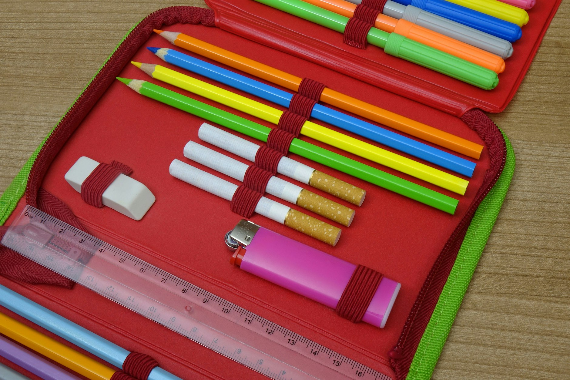 In einer Federmappe liegen neben Buntstiften drei Zigaretten und ein Feuerzeug.