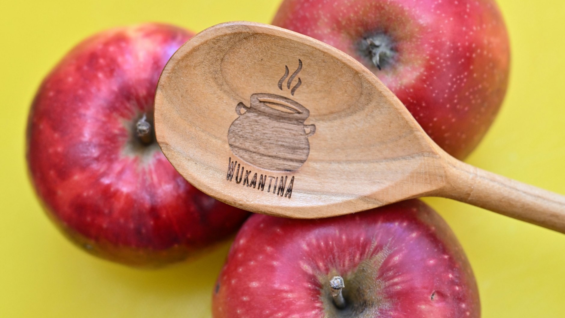 Ein Holzlöffel mit dem Logo der Wukantina liegt auf Äpfeln in der Küche.