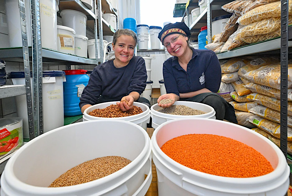 PRODUKTION - Franziska Ernst (l) und Annette Schmidt, beide leiten die Wukantina, sind im Lager mit Behältern voller Getreide, Linsen und Nüssen zu sehen.  