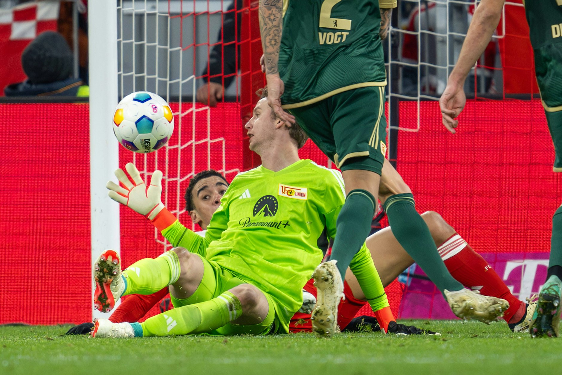 Jamal Musiala von Bayern München liegt auf der Torlinie, Unions Torwart Frederik Ronnow fängt den Ball.  