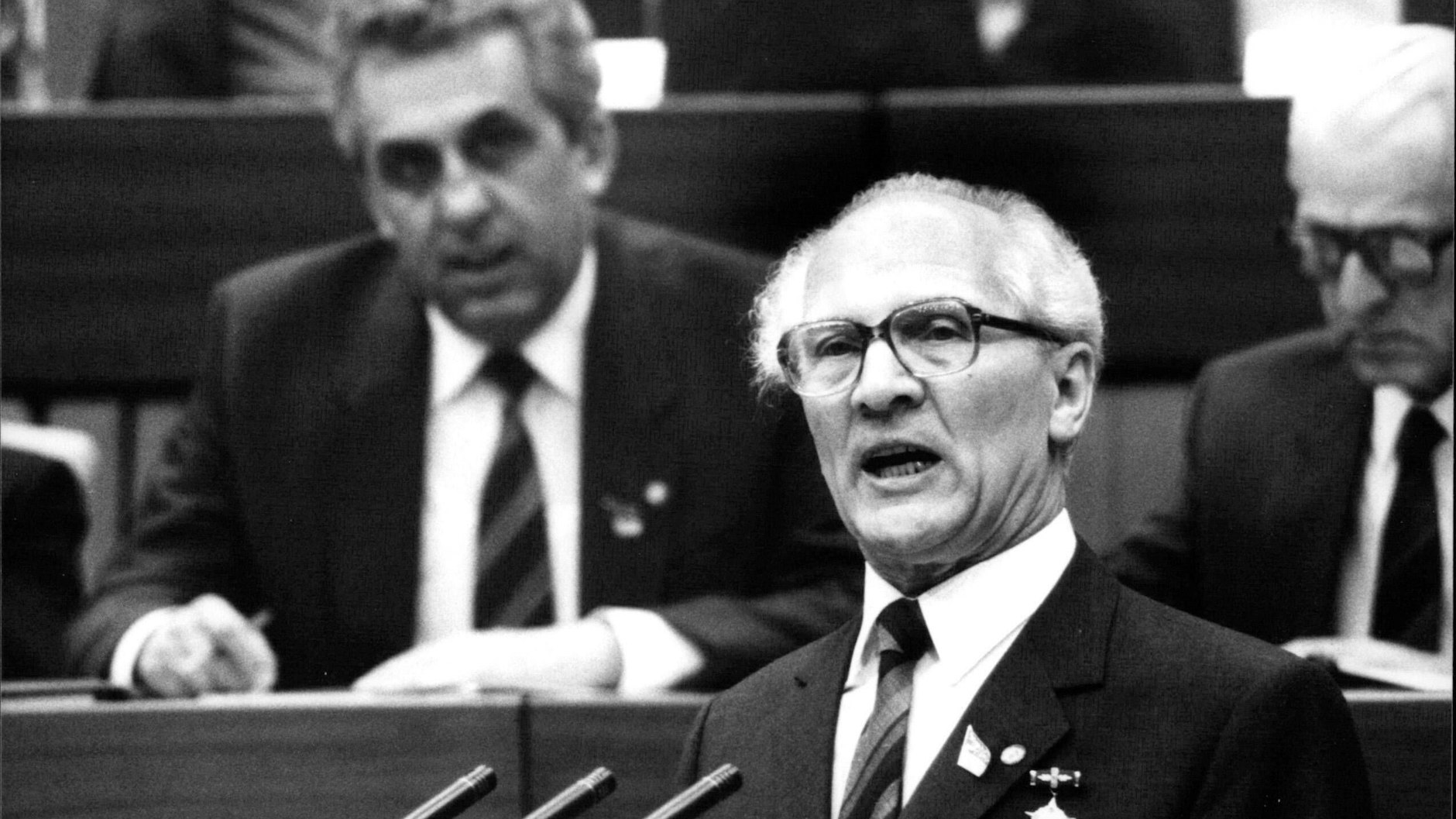 Erich Honecker hält eine Rede auf dem SED-Parteitag (1986): Hinter ihm im Podium sitzt das damalige Politbüro-Mitglied Egon Krenz, der als Honeckers-Kronprinz gehandelt wurde.&nbsp;