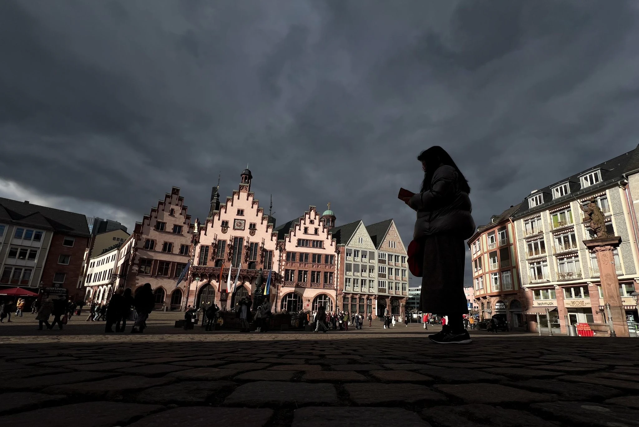 Während sich die dunklen Wolken über Frankfurt ziehen, leuchtet das Rathaus Römer im Sonnenschein.  